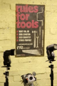 Two flash guns in front of a poster on a wall which reads "Rules for tools"