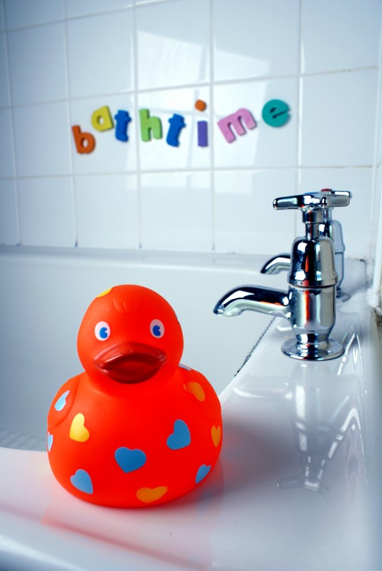 Bath time A rubber duck on the edge of a bath next to some taps, behind are letters stuck to some tiles that read 'bath time'